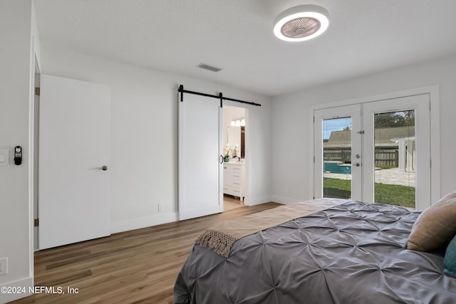 bedroom featuring french doors, a barn door, access to exterior, hardwood / wood-style floors, and ensuite bathroom