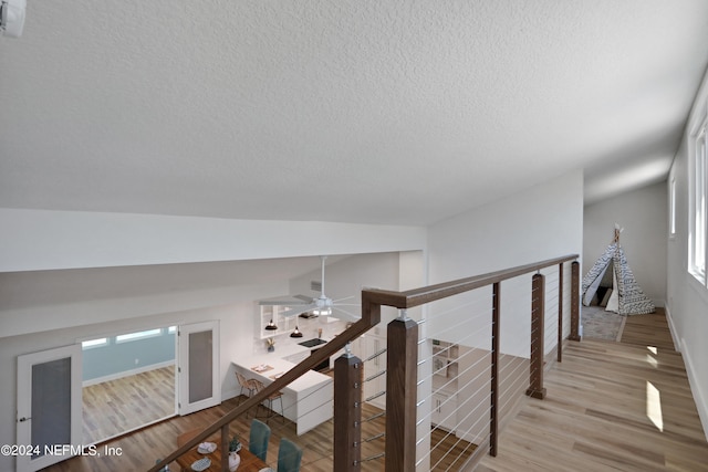 hall featuring light wood-type flooring, a textured ceiling, and vaulted ceiling