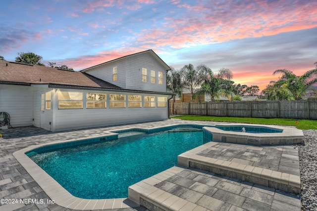 pool at dusk featuring a patio and an in ground hot tub