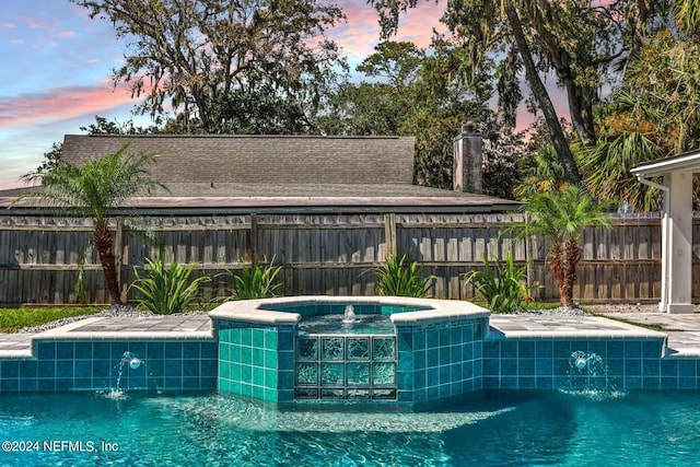 pool at dusk with pool water feature and an in ground hot tub