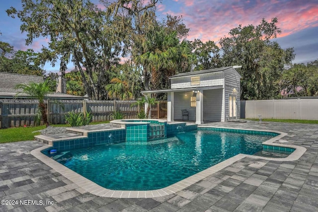 pool at dusk featuring a patio area and an in ground hot tub