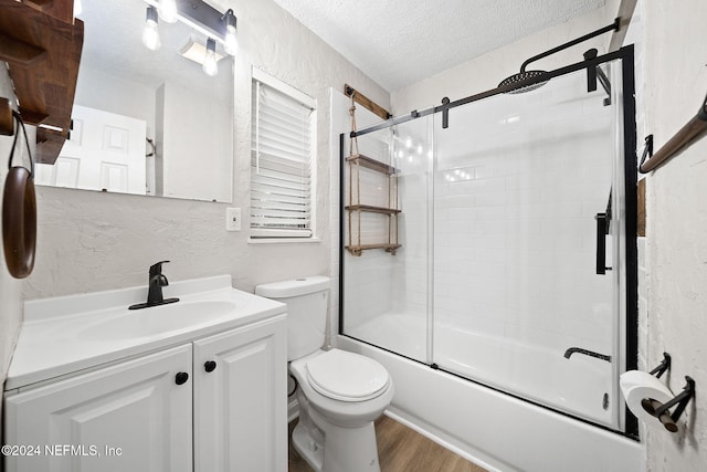 full bathroom with combined bath / shower with glass door, hardwood / wood-style floors, a textured ceiling, toilet, and vanity