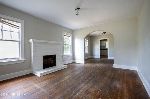 unfurnished living room with a brick fireplace and dark hardwood / wood-style floors