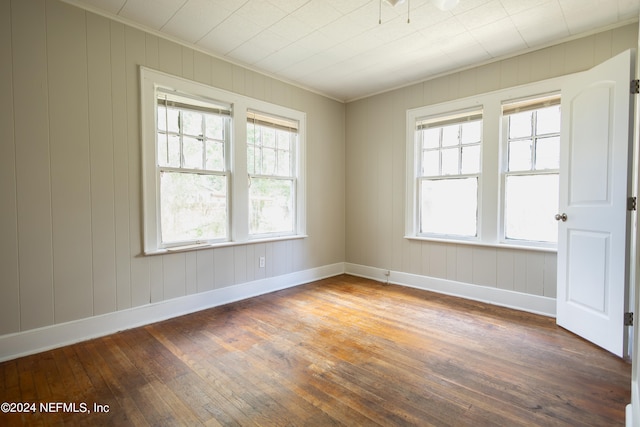 spare room featuring ornamental molding, wooden walls, and dark wood-type flooring