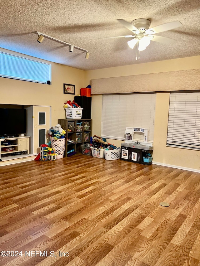 recreation room with a textured ceiling, rail lighting, ceiling fan, and hardwood / wood-style flooring