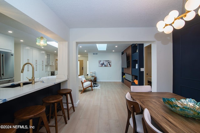 dining space featuring light wood-type flooring, a skylight, a textured ceiling, and sink