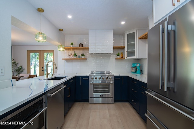 kitchen with blue cabinetry, premium appliances, light stone countertops, sink, and white cabinets