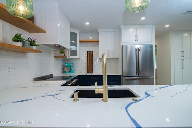 kitchen featuring tasteful backsplash, stainless steel refrigerator, light stone countertops, sink, and white cabinets