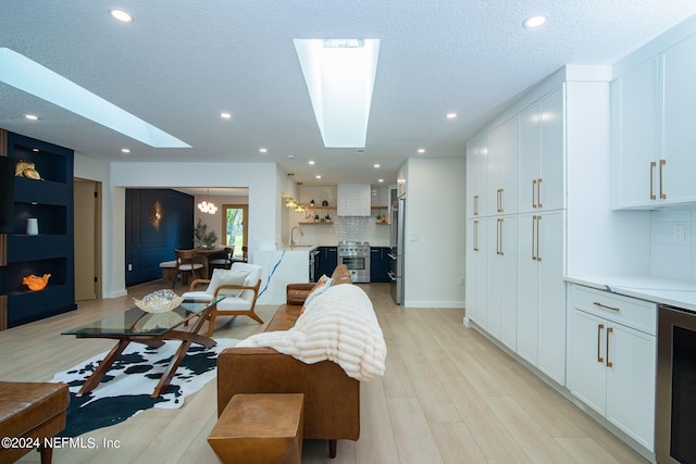 living room featuring a textured ceiling, sink, a skylight, light hardwood / wood-style flooring, and wine cooler