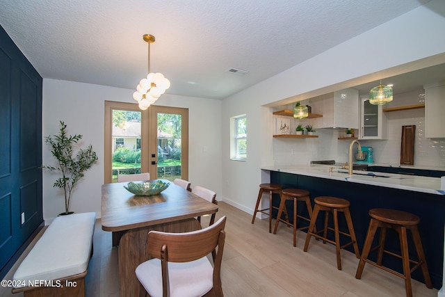 dining room with a textured ceiling, sink, french doors, and light hardwood / wood-style flooring