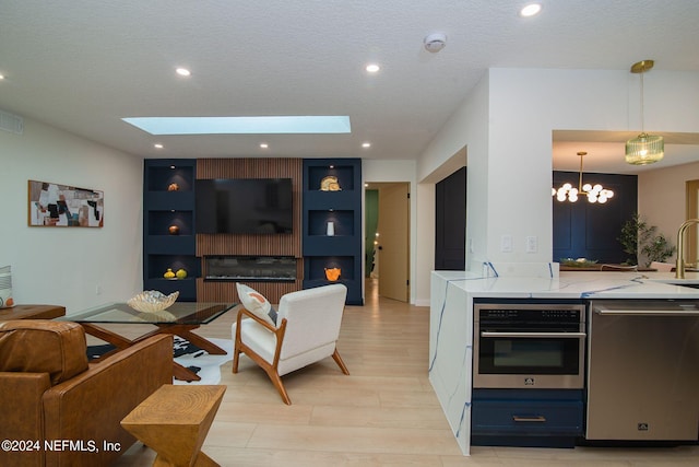 living room featuring light hardwood / wood-style floors, an inviting chandelier, a textured ceiling, sink, and a skylight