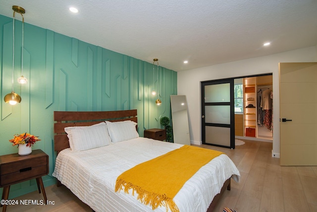 bedroom featuring a closet, a walk in closet, hardwood / wood-style floors, and a textured ceiling