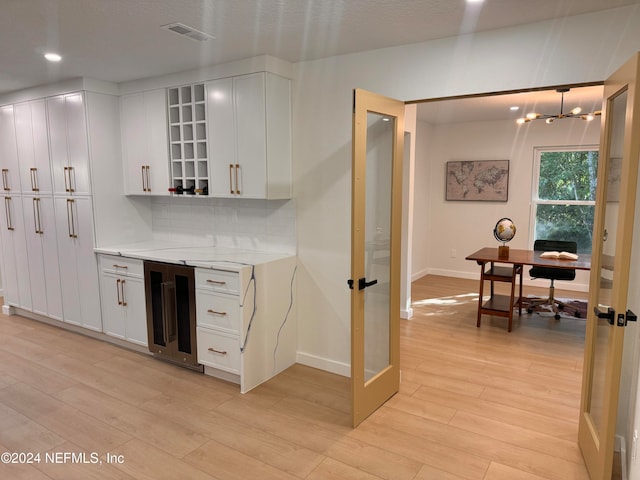 kitchen featuring white cabinets, light hardwood / wood-style floors, light stone counters, and wine cooler