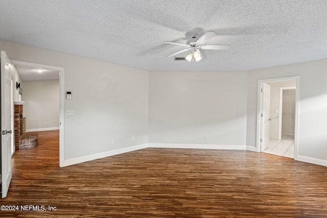 spare room with a textured ceiling, a brick fireplace, wood-type flooring, and ceiling fan