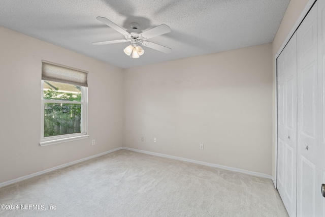 unfurnished bedroom featuring a closet, a textured ceiling, light colored carpet, and ceiling fan