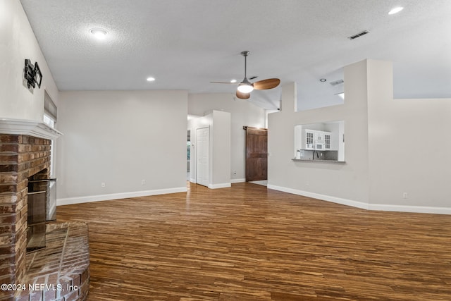 unfurnished living room featuring ceiling fan, a textured ceiling, hardwood / wood-style flooring, high vaulted ceiling, and a brick fireplace