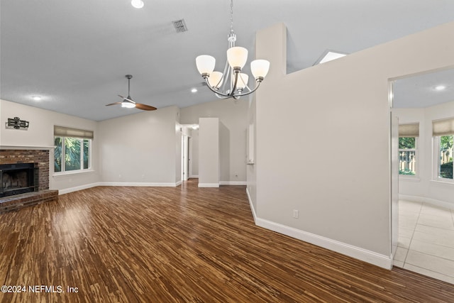 unfurnished living room with vaulted ceiling, a brick fireplace, wood-type flooring, and ceiling fan with notable chandelier