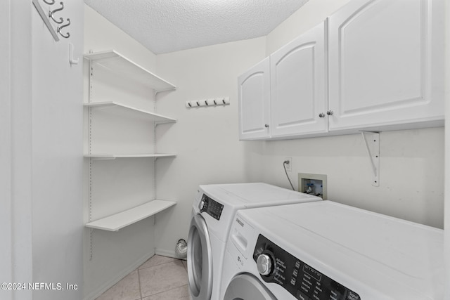 laundry room with a textured ceiling, washing machine and dryer, light tile patterned floors, and cabinets