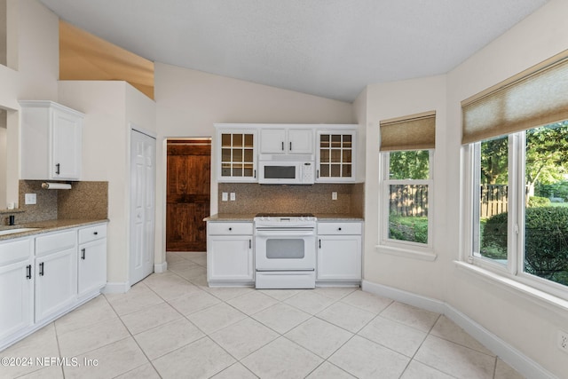 kitchen with white cabinets, backsplash, vaulted ceiling, light stone counters, and white appliances