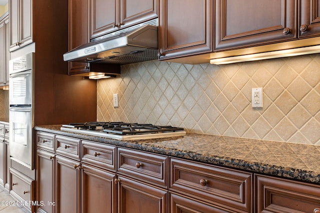 kitchen featuring dark stone countertops, stainless steel appliances, tasteful backsplash, and range hood