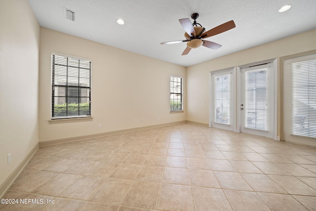 empty room with a textured ceiling, a healthy amount of sunlight, light tile patterned flooring, and ceiling fan