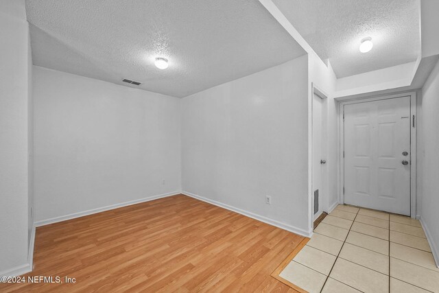 unfurnished room featuring light wood finished floors, a textured ceiling, visible vents, and baseboards
