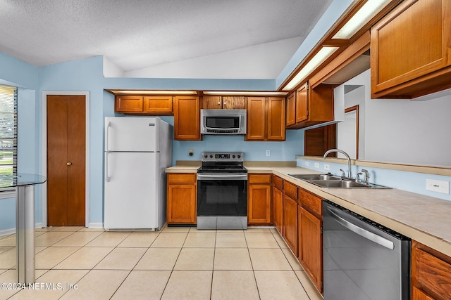 kitchen featuring brown cabinets, a sink, stainless steel appliances, vaulted ceiling, and light countertops