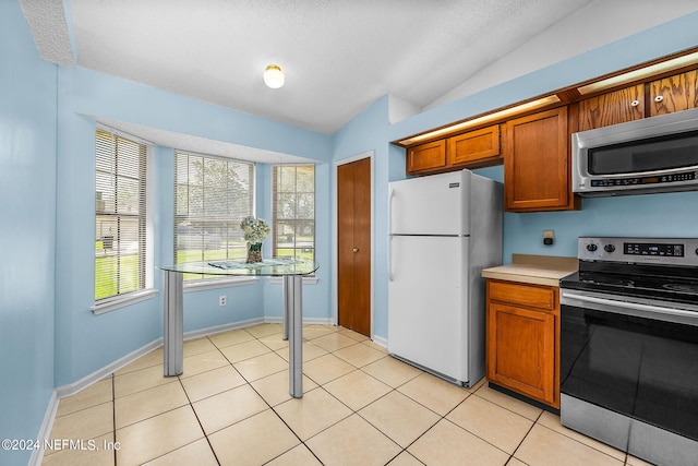 kitchen with brown cabinets, light tile patterned floors, light countertops, appliances with stainless steel finishes, and lofted ceiling