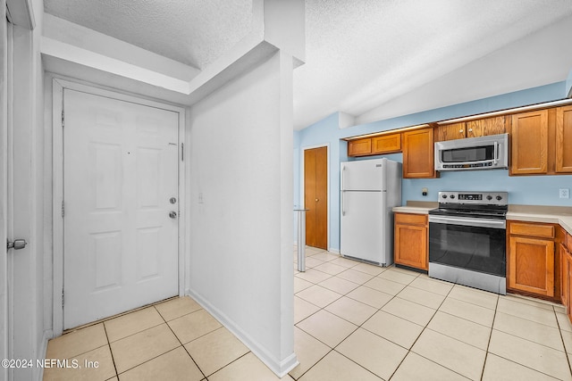 kitchen with light tile patterned flooring, stainless steel appliances, a textured ceiling, and lofted ceiling