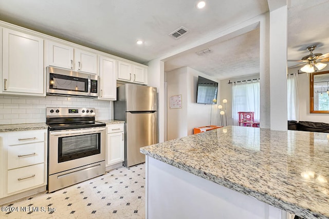 kitchen featuring light stone counters, white cabinets, backsplash, appliances with stainless steel finishes, and ceiling fan