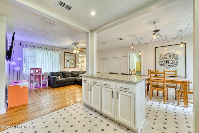 kitchen with light wood-type flooring, light stone counters, a textured ceiling, ceiling fan with notable chandelier, and white cabinets