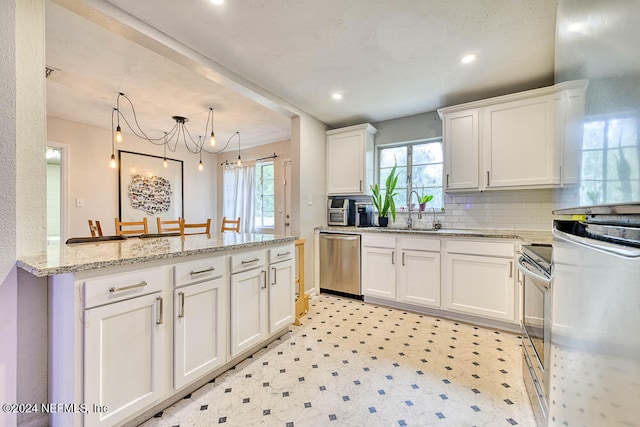 kitchen with white cabinetry, kitchen peninsula, light stone countertops, stainless steel appliances, and sink