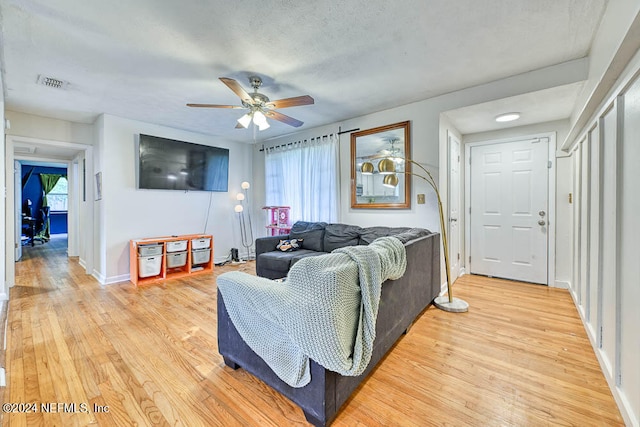 living room with light hardwood / wood-style flooring, ceiling fan, plenty of natural light, and a textured ceiling