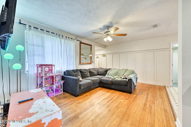 living room featuring ceiling fan, a textured ceiling, and light wood-type flooring