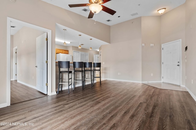 unfurnished living room with a towering ceiling, ceiling fan, and dark wood-type flooring