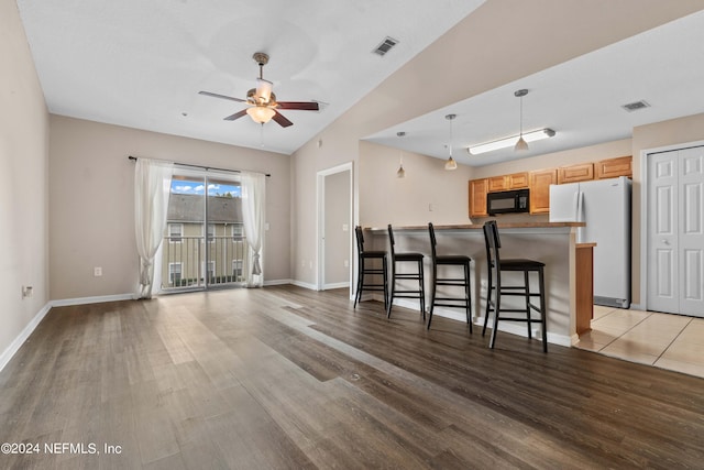 kitchen featuring white refrigerator, lofted ceiling, decorative light fixtures, light wood-type flooring, and a kitchen bar