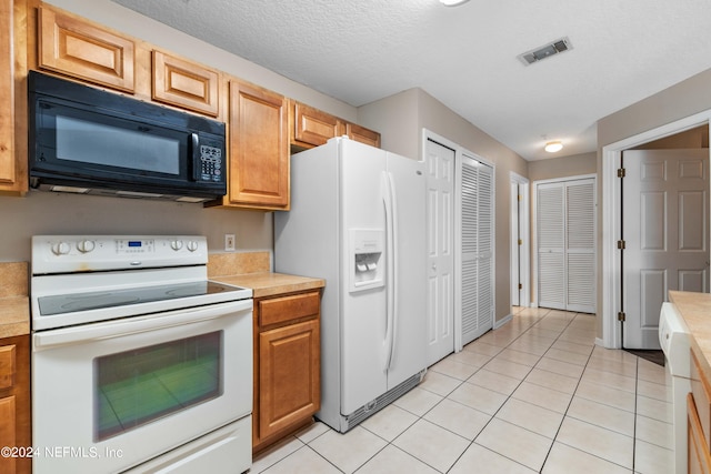 kitchen with a textured ceiling, white appliances, and light tile patterned floors