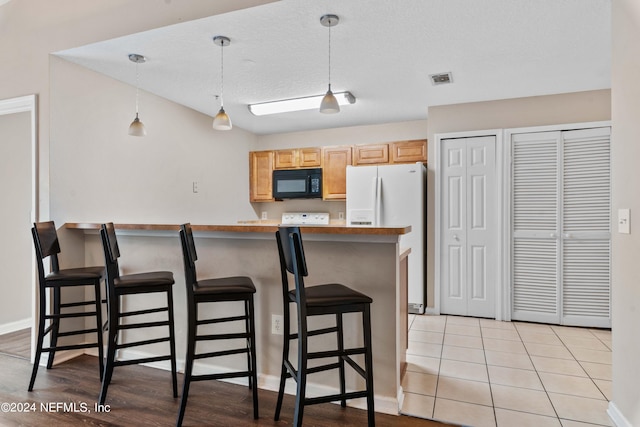 kitchen with hanging light fixtures, a breakfast bar, light brown cabinets, light tile patterned floors, and white fridge with ice dispenser