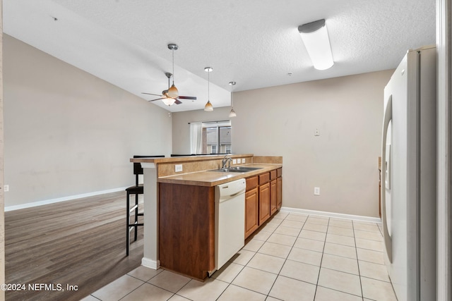 kitchen with kitchen peninsula, white appliances, sink, a breakfast bar area, and vaulted ceiling