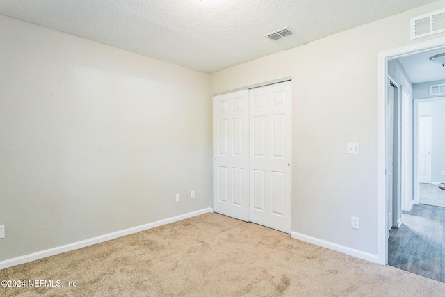 unfurnished bedroom with light colored carpet, a textured ceiling, and a closet