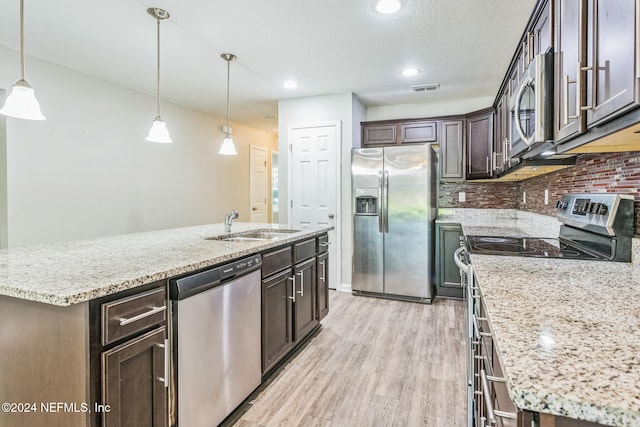 kitchen featuring an island with sink, light wood-type flooring, hanging light fixtures, appliances with stainless steel finishes, and dark brown cabinets