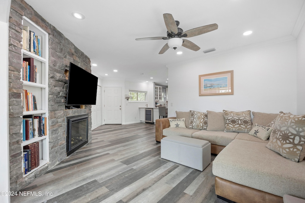 living room featuring ceiling fan, built in shelves, ornamental molding, a fireplace, and light wood-type flooring