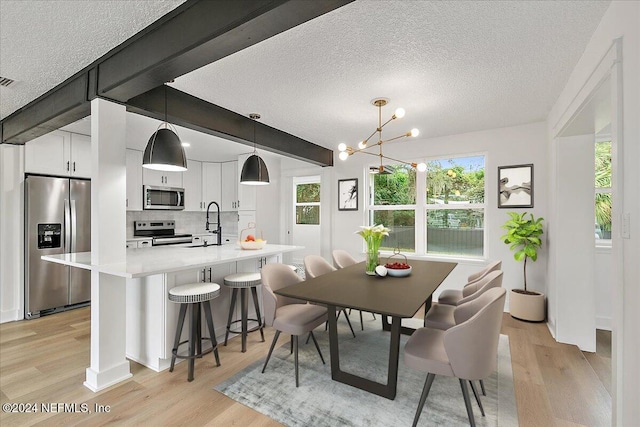 dining room featuring a notable chandelier, light wood-type flooring, a textured ceiling, and a healthy amount of sunlight