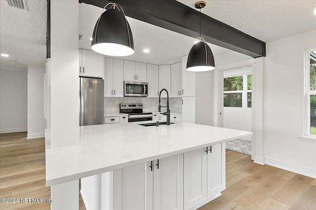 kitchen with white cabinets, pendant lighting, sink, a textured ceiling, and stainless steel appliances