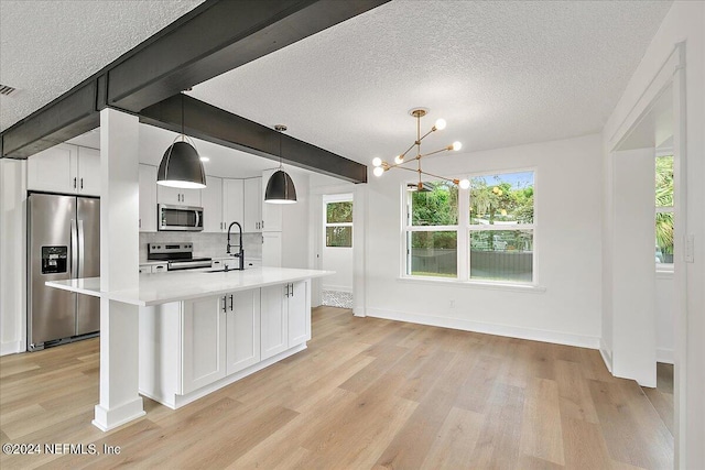 kitchen featuring an island with sink, hanging light fixtures, a textured ceiling, white cabinetry, and appliances with stainless steel finishes