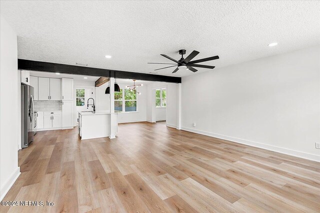 unfurnished living room featuring a textured ceiling, sink, and light hardwood / wood-style flooring