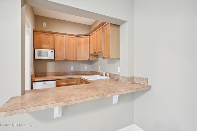 kitchen with white appliances, sink, kitchen peninsula, and a kitchen breakfast bar