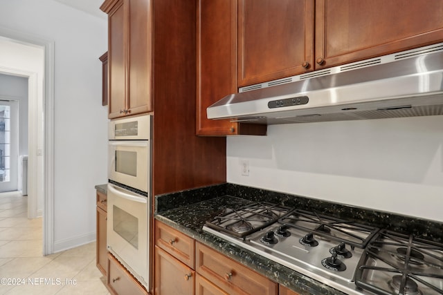 kitchen with dark stone countertops, light tile patterned floors, double oven, and stainless steel gas stovetop