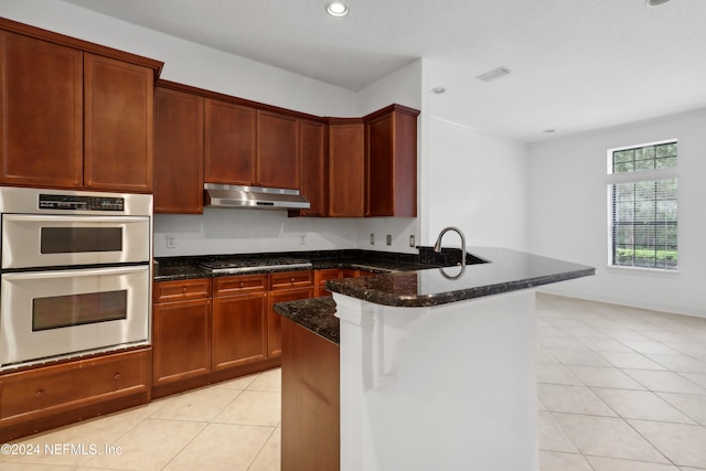 kitchen featuring appliances with stainless steel finishes, kitchen peninsula, light tile patterned floors, and dark stone countertops