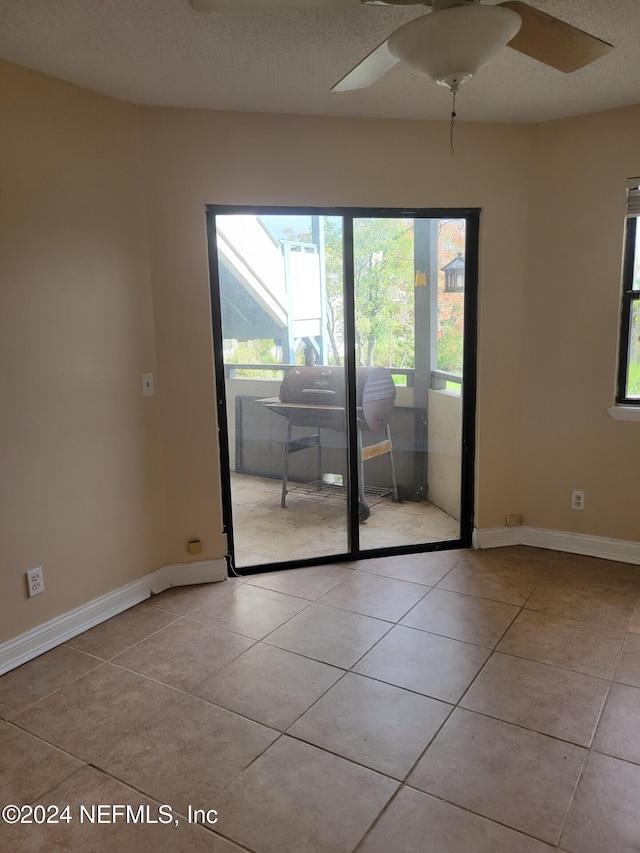 empty room with ceiling fan, a textured ceiling, and light tile patterned floors